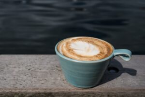 Blue ceramic cup of latte on a weathered wooden dock with water in the background