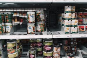 Shelves of assorted canned foods in a grocery store stacked in rows on a refrigerated display